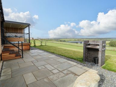 A patio with tiled flooring a brick barbecue a wooden staircase and a railing overlooking a grassy field at Math Lodge 3 in Llanelidan near Corwen