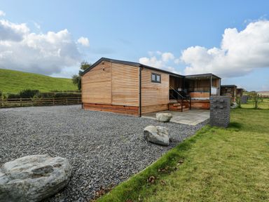 A wooden lodge with a gravel driveway and a small patio area at Math Lodge 3 in Llanelidan near Corwen