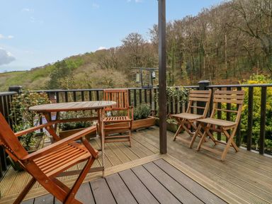 A wooden deck with a round table and four chairs surrounded by trees and plants at 22 Two Little Ducks in Lynton