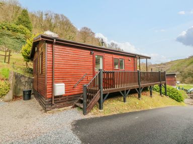 A wooden cabin with a small porch and stairs on a hillside next to a paved road at 22 Two Little Ducks in Lynton