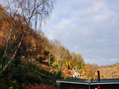 A hillside with trees and a house near a rooftop under a cloudy sky at 22 Two Little Ducks in Lynton
