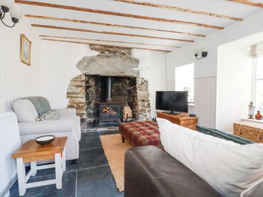 A living room with a wood burning stove in a stone fireplace two sofas a wooden side table and a television on a wooden cabinet at Hilldene in Treknow
