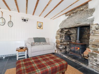 A living room with a stone fireplace and a wood burning stove a plaid ottoman a beige sofa and two round mirrors on the wall at Hilldene in Treknow