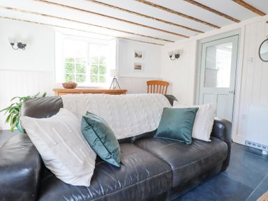 A living room with a black leather sofa and cushions in front of a window with wooden beams on the ceiling at Hilldene in Treknow