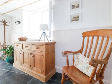 A wooden chair with a cushion next to a wooden cabinet with a lamp and a woven basket on top in a room at Hilldene in Treknow