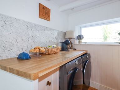 A laundry room with a wooden countertop washing machine dryer basket with scones and a coffee machine at Hilldene in Treknow
