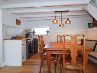 A dining area with wooden table and chairs next to a countertop with washing machine and dryer under a window at Hilldene Treknow