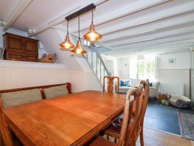 A dining area with wooden table and chairs next to a living area with armchairs under a window at Hilldene in Treknow