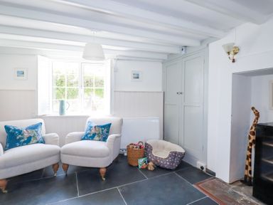 A sitting area with two armchairs with blue pillows a window with shutters a pet bed a basket and a wooden giraffe at Hilldene in Treknow