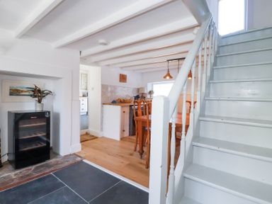 A dining area with wooden table and chairs next to a staircase and a small fridge in a white room at Hilldene Treknow