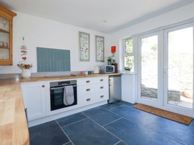 A kitchen with white cabinets wooden countertops a black oven a microwave and glass doors leading outside at Hilldene in Treknow