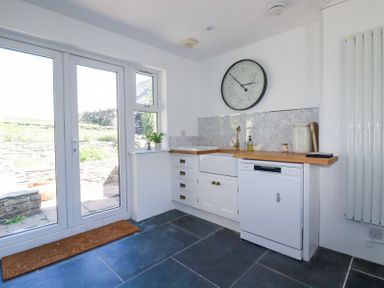 A kitchen with white cabinets wooden countertops a large round wall clock and glass doors at Hilldene in Treknow