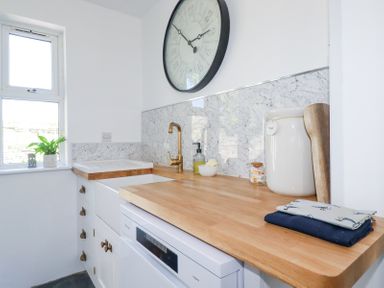A kitchen counter with a wooden countertop a white sink gold faucet a large wall clock and kitchen accessories at Hilldene in Treknow