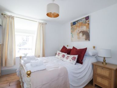A bedroom with a bed with red and floral pillows bedside tables with lamps and curtains on the window at Hilldene in Treknow