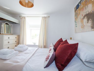 A bedroom with a bed with red and patterned pillows a window with curtains and a dresser with a mirror at Hilldene Treknow