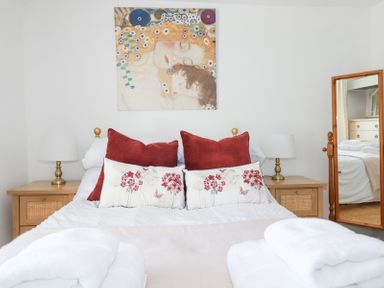 A bedroom with a bed with pillows and lamps on wooden bedside tables and a mirror reflecting a dresser at Hilldene in Treknow