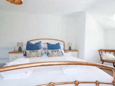 A bedroom with a metal framed bed white bedding blue and patterned pillows two bedside tables with lamps and a wooden chair with a pillow at Hilldene in Treknow