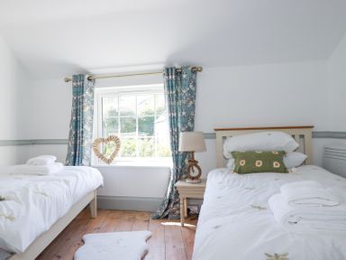 A bedroom with two single beds a window with curtains a bedside table and a lamp at Hilldene in Treknow