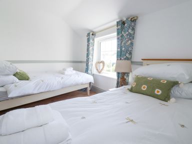 A bedroom with two beds white bedding and green pillows by a window with blue floral curtains at Hilldene in Treknow
