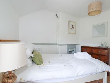 A bedroom with a bed with white bedding and green pillow a wooden dresser and a lamp at Hilldene in Treknow