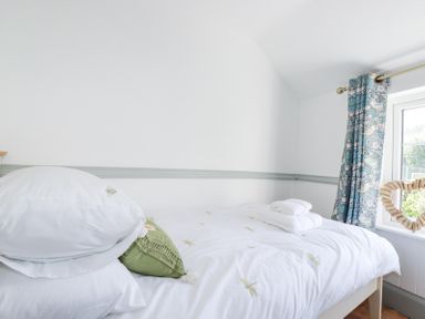 A single bed with white bedding and folded towels near a window with patterned curtains at Hilldene in Treknow
