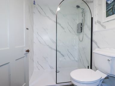 A bathroom with a white toilet and a glass shower enclosure with marble patterned walls at Hilldene in Treknow