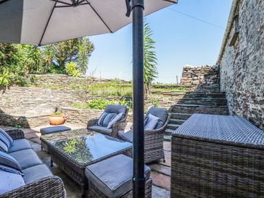 An outdoor patio with a wicker sofa set and table under a large umbrella next to stone walls and steps at Hilldene in Treknow