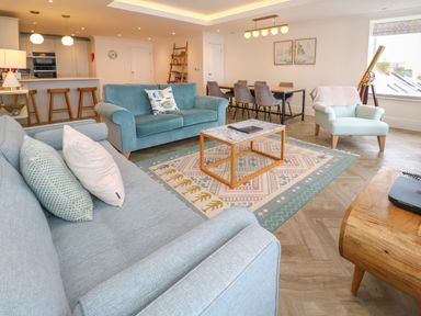 A living room with sofas a coffee table a dining table and chairs and a kitchen area with bar stools at Amelias Point in St Ives