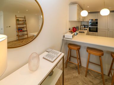 A kitchen with a white countertop and wooden bar stools next to a table with a clear vase and plates at Amelia's Point in St Ives