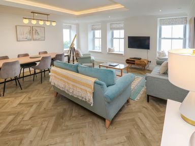 A living room and dining area with blue sofas dining table and chairs wall art and television at Amelia's Point in St Ives