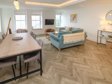 A living room with a dining table and chairs a blue sofa a coffee table wall art a round mirror and a telescope at Amelia's Point in St Ives