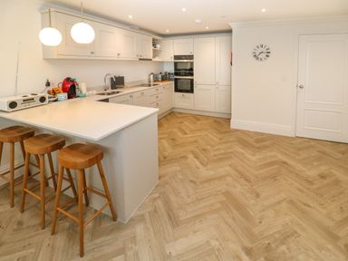 A kitchen with white cabinets a countertop bar with three wooden stools and wooden herringbone floor at Amelia's Point in St Ives