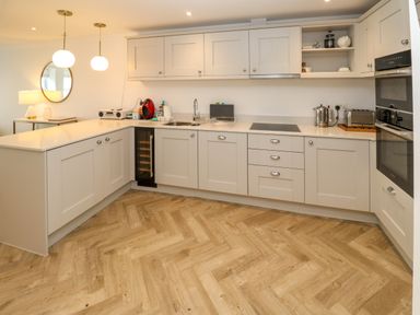A kitchen with white cabinets wooden floor and various appliances at Amelias Point in St Ives
