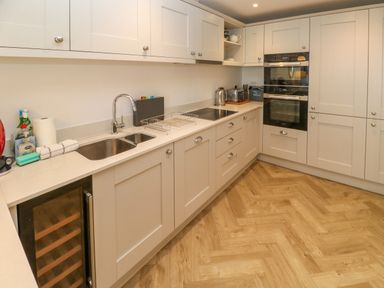 A kitchen with white cabinets a double sink a wine cooler and built in ovens at Amelia's Point in St Ives
