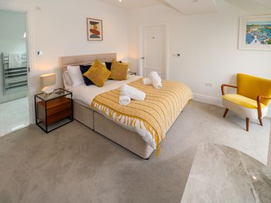 A bedroom with a bed with folded towels bedside tables a yellow chair and wall art at Amelia's Point in St Ives