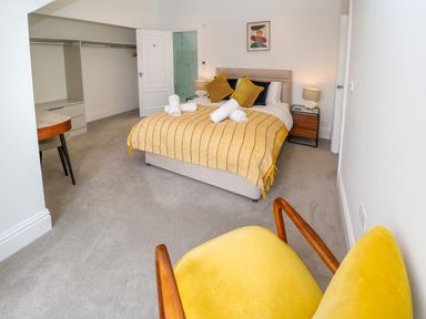 A bedroom with a bed with yellow pillows and blanket a yellow chair a bedside table with lamp and an open closet at Amelias Point in St Ives