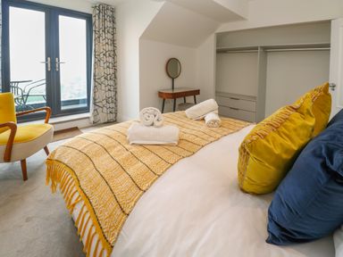A bedroom with a bed covered in a yellow blanket and pillows near a yellow chair and balcony doors at Amelias Point in St Ives