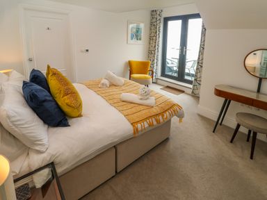 A bedroom with a bed with pillows and towels a yellow armchair a dressing table with a round mirror and glass doors leading to a balcony at Amelias Point in St Ives