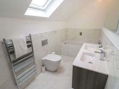 A bathroom with a double sink vanity a bathtub a wall mounted toilet a heated towel rack and a skylight at Amelia's Point in St Ives