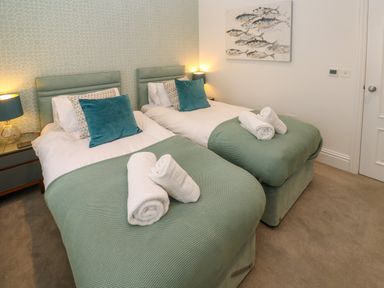 A bedroom with two single beds each with green covers and rolled white towels at Amelia's Point in St Ives