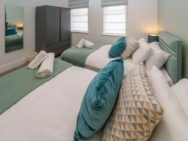 A bedroom with two beds with green throws and pillows a wardrobe and a mirror on the wall at Amelias Point in St Ives