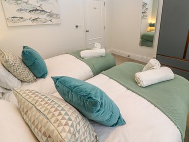 A bedroom with two beds with green throws and pillows and rolled towels on top at Amelia's Point in St Ives