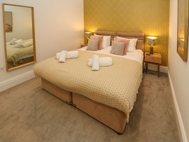 A bedroom with a double bed with cushions and rolled towels bedside tables with lamps and a large mirror at Amelia's Point in St Ives