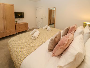 A bedroom with a bed with pillows and rolled towels a wooden wardrobe a chest of drawers and a wall mirror at Amelias Point in St Ives