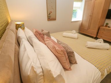 A bedroom with a bed with multiple pillows rolled towels on a patterned blanket a wardrobe and chest of drawers with a small plant at Amelias Point in St Ives