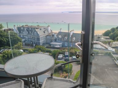 A balcony with a glass table and chair overlooking buildings and a beach at Amelias Point in St Ives