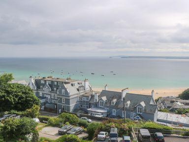 A coastal view with buildings and parked cars near a beach with boats on the water at Amelias Point in St Ives