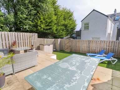 An outdoor patio with a weathered table two blue lounge chairs wicker furniture and a wooden fence at Amelias Point in St Ives