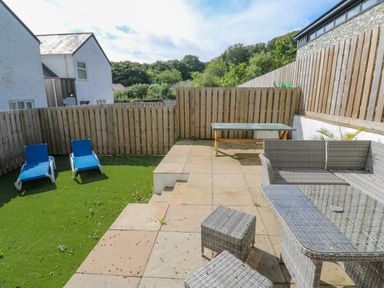 An outdoor patio area with wicker furniture a table two blue lounge chairs and a wooden fence at Amelias Point in St Ives
