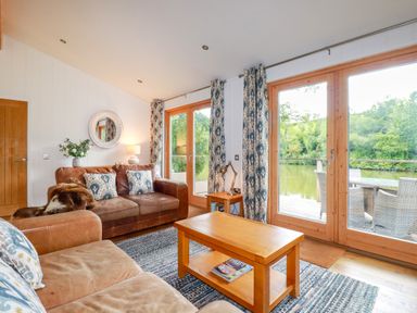 A living room with leather sofas wooden coffee table and large glass doors overlooking water at 10 Water's Edge in Lanreath